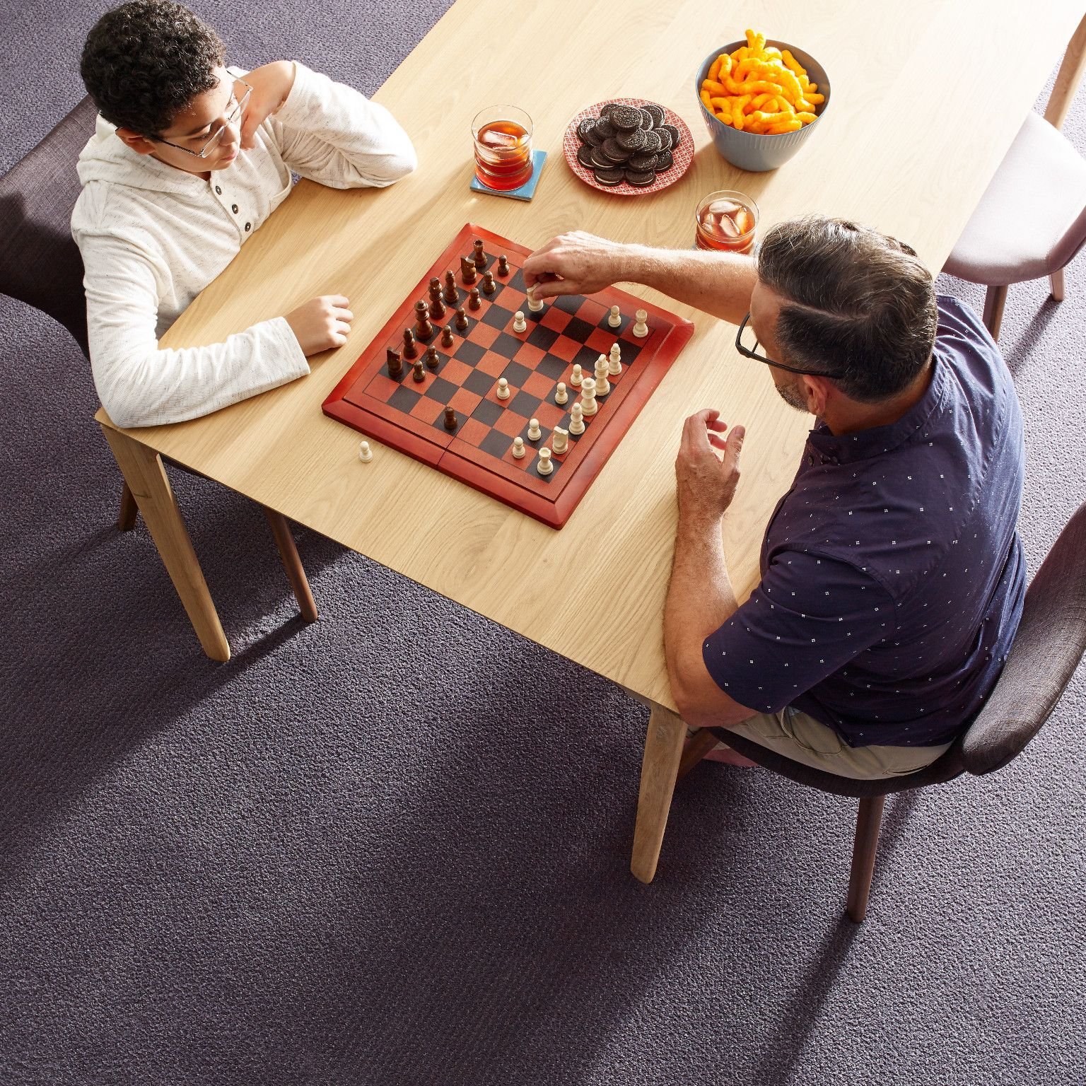 Two people playing chess at a wooden table in a room with purple carpet from Carpet Villa in Grand Rapids, MI