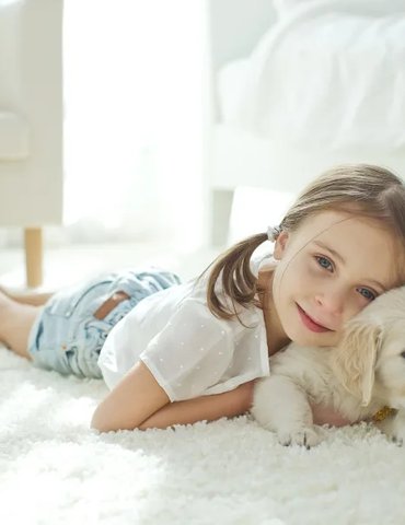 Young girl laying on a small golden retriever puppy