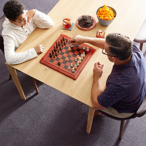 Two people playing chess at a wooden table in a room with purple carpet from Carpet Villa in Grand Rapids, MI